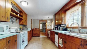 A kitchen with wooden cabinets, a white dishwasher, and a countertop with various appliances. - Cozy Cape style home near the beach and ferry with patio, W/D, & AC (Hyannis)