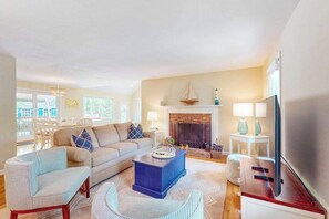 Ein Wohnzimmer mit einer Couch, Sesseln, einem Couchtisch, einem Kamin und einem Fernseher.