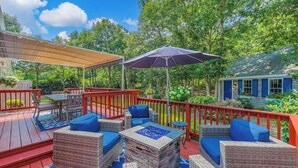 A covered outdoor deck with wicker furniture, a small table, and a large umbrella. - Peaceful beach retreat: private yard, close to beaches, Chatham & rail trail (Harwich)
