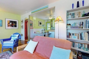 A cozy living room with a sofa, a chair, a bookshelf, and a dining area visible through an archway. - Lakefront Cottage with a Deck, Free WiFi, Gas Grill - Close to Ferries & Beaches (Oak Bluffs)