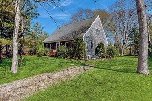 Une maison de plain-pied avec un toit à pignon, entourée d’une pelouse bien entretenue et d’arbres.