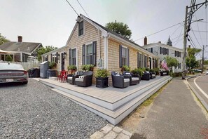 A two-story house with a front porch, outdoor seating, and a flag. - Stylish coastal retreat with modern chef's kitchen, private yard, and fire pit (Provincetown)