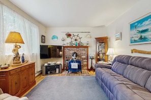 A living room with a fireplace, a sofa, a television, and nautical decorations. - Cape Cod charmer with a large yard, deck, grill, beach gear, & central AC (Hyannis)