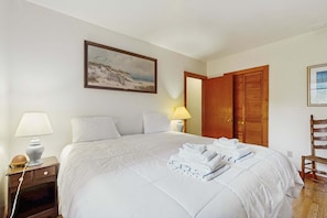 A hotel room with a bed, a nightstand, a lamp, a painting, and a wooden door. - Cape Cod charmer with a large yard, deck, grill, beach gear, & central AC (Hyannis)