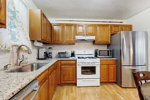 A kitchen with wooden cabinets, a stainless steel refrigerator, a microwave, a stove, and a sink. - Cape Cod charmer with a large yard, deck, grill, beach gear, & central AC (Hyannis)
