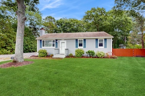 A single-story house with a front porch, a chimney, and a well-maintained lawn. - Cape Cod charmer with a large yard, deck, grill, beach gear, & central AC (Hyannis)