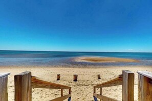 Ein Strand mit hölzernen Stegen, die zum Wasser führen, ein klarer Himmel und ruhiges Meer.