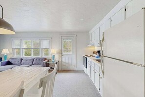 Eine kleine Küche mit weißen Schränken, einem Kühlschrank, einem Esstisch und einer Couch.