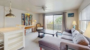 Een woonkamer met een bank, een eettafel, een plafondventilator en een groot raam met gordijnen.
