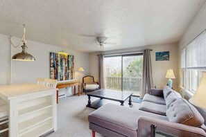 Ein Wohnzimmer mit einer Couch, einem Esstisch, einem Deckenventilator und einem großen Fenster mit Vorhängen.