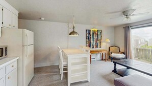 Een kamer met een eettafel, stoelen, een plafondventilator, een schilderij en uitzicht door een raam.