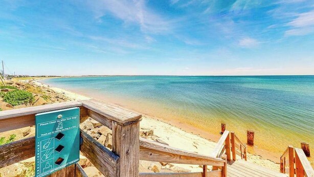 Een strand met een houten looppad en een bordje met de instructie om na honden op te ruimen.