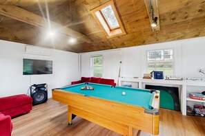 A pool table in a room with wooden ceilings, a red couch, a TV, and a window. - Pond Treasure: Private beach, hot tub, sauna, play area & dog-friendly (Sandwich)