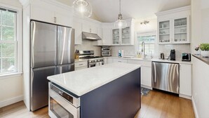 Een moderne keuken met roestvrijstalen apparatuur, witte kasten en hanglampen.