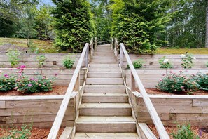 A wooden staircase with railings leading up a slope, surrounded by raised garden beds with flowering plants. - Pond Treasure: Private beach, hot tub, sauna, play area & dog-friendly (Sandwich)