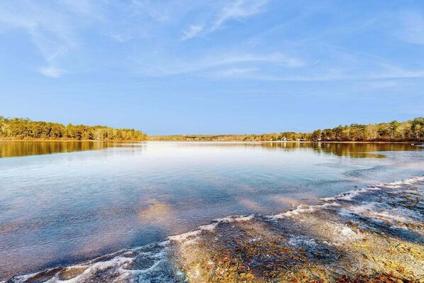 A calm lake with a clear sky, surrounded by trees. - Pond Treasure: Private beach, hot tub, sauna, play area & dog-friendly (Sandwich)