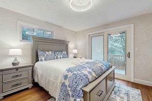A bedroom with a bed, nightstands, a dresser, a chandelier, and a sliding glass door. - Pond Treasure: Private beach, hot tub, sauna, play area & dog-friendly (Sandwich)
