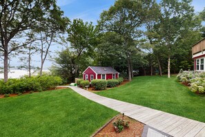 A red house with a wooden deck and a lawn. - Pond Treasure: Private beach, hot tub, sauna, play area & dog-friendly (Sandwich)