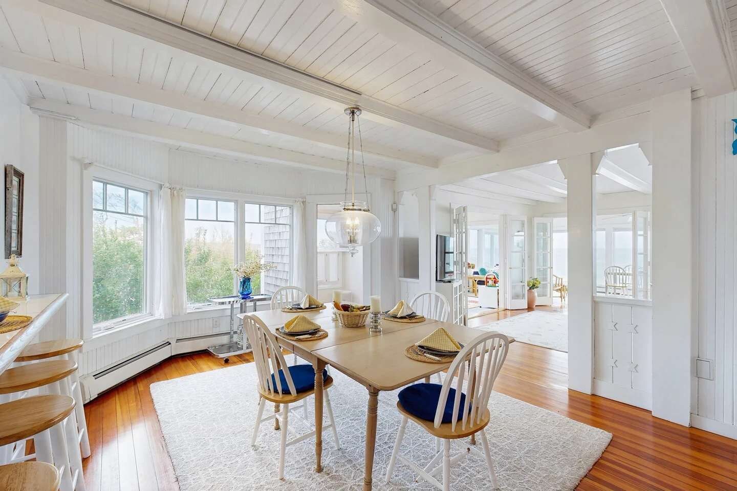 A spacious dining area with a large table, white chairs, and a chandelier.