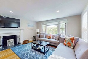 A living room with a fireplace, sofa, coffee table, and television. - Updated Retreat w/ Lots of Perks: Big Yard, Canoe, Bikes Stroll to Long Pond (South Yarmouth)