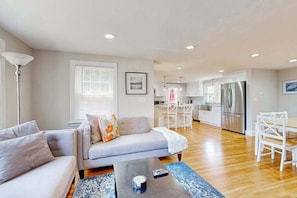 A modern living room with a sofa, coffee table, and a dining area with a table and chairs. - Updated Retreat w/ Lots of Perks: Big Yard, Canoe, Bikes Stroll to Long Pond (South Yarmouth)