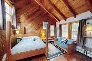 A wooden cabin interior with a bed, a sofa, and a desk.