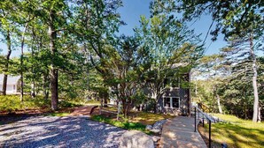A pathway leading to a building surrounded by trees and a gravel area. - Serene Home on 3 Acres w/ Wraparound Deck & Pool Table - Close to Beaches (Wellfleet)
