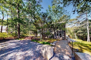 A pathway leading to a building surrounded by trees and a gravel area.