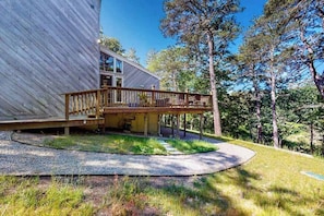 A modern house with a wooden deck, surrounded by trees.