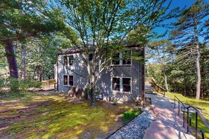 A two-story house with a deck, surrounded by trees.