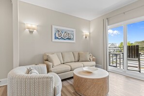 Una sala de estar con un sofá color beige, una mesa redonda de centro, un sillón estampado y un cuadro en la pared.