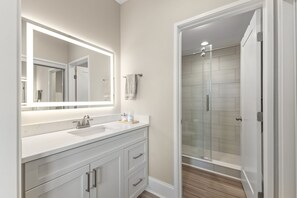 Un baño con un espejo grande, un lavabo y una ducha con mampara de vidrio.