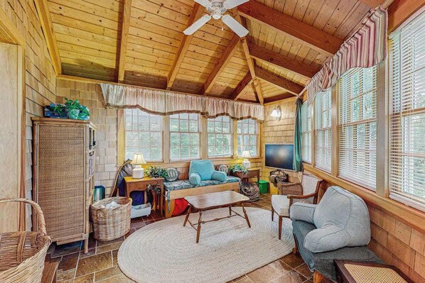A cozy cabin interior with a wooden ceiling, a sofa, a television, and large windows.
