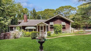 A two-story house with a front porch, a chimney, and a well-maintained lawn. - Beautiful Estate with Large Lawn Made for Socializing and Kids' Playroom (Vineyard Haven)