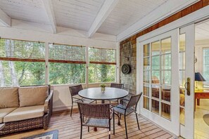 A covered patio with a round table and chairs, a sofa, and a view through the windows.