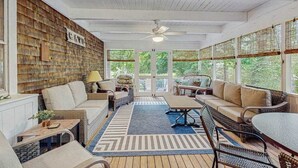A sunroom with wicker furniture, a ceiling fan, and large windows. - Beautiful Estate with Large Lawn Made for Socializing and Kids' Playroom (Vineyard Haven)