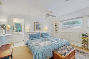 A bedroom with a bed, bedside table, lamp, ceiling fan, window, and dresser.