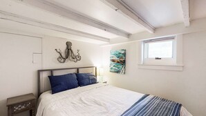 A bedroom with a bed, a nightstand, a window, and wall art. - Modern & bright condo with patio, W/D, and central location near town & beach (Provincetown)