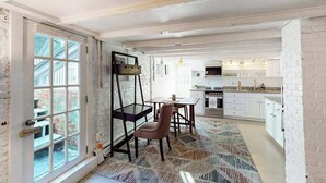 A spacious room with a large window, a dining area with a table and chairs, and a kitchen area with cabinets and appliances. - Modern & bright condo with patio, W/D, and central location near town & beach (Provincetown)