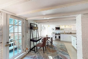 A spacious room with a large window, a dining area with a table and chairs, and a kitchen area with cabinets and appliances. - Modern & bright condo with patio, W/D, and central location near town & beach (Provincetown)