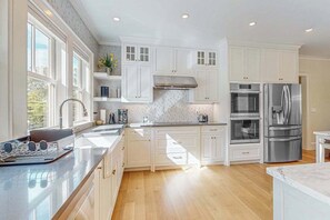 A modern kitchen with white cabinetry, stainless steel appliances, and a large window providing natural light.