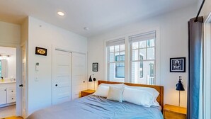 Ein Schlafzimmer mit einem Bett, zwei Nachttischen, einem Fenster und einer Tür.