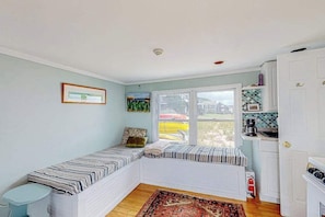 A room with a built-in bench, a window with a view, a small kitchen area, and a door.