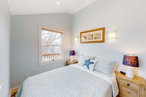 A bedroom with a bed, two bedside tables, a window, and wall-mounted lamps. - Freestanding cottage with decks, steps from Commercial Street & the beach (Provincetown)