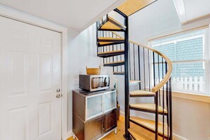 A spiral staircase with a wooden finish, a white door, and a small cabinet with a microwave on top. - Freestanding cottage with decks, steps from Commercial Street & the beach (Provincetown)