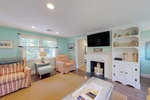 A living room with a sofa, armchair, fireplace, TV, and shelves. - Remodeled home w/beach pass & new furnishings on 1-acre parcel - steps to lake (Centerville)