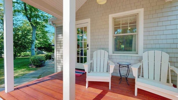 Eine Veranda mit zwei Adirondack-Stühlen, einem kleinen runden Tisch und einem Fenster mit Blick auf den Garten.