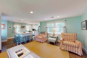 A living room with a kitchen in the background, a striped armchair, a small table with a lamp, and a bar stool. - Remodeled home w/beach pass & new furnishings on 1-acre parcel - steps to lake (Centerville)