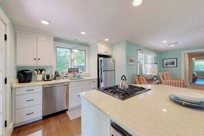 A kitchen with white cabinets, a stainless steel refrigerator, a gas stove, and a sign that reads 'Welcome to Cottage.' - Remodeled home w/beach pass & new furnishings on 1-acre parcel - steps to lake (Centerville)