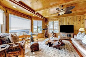 Ein Holzinnenraum mit einem großen Fernseher, einem Deckenventilator und Blick durch die Fenster.